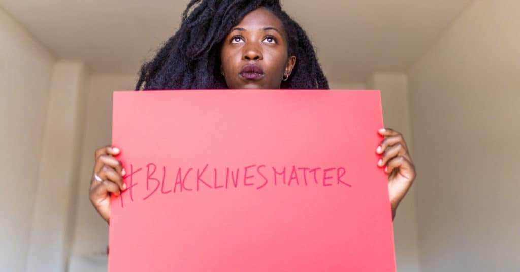 Young black woman holding "Black Lives Matter" banner indoors