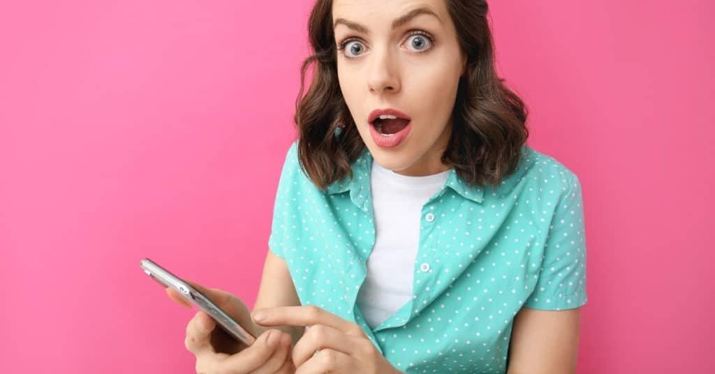 surprised young woman with mobile phone on color background