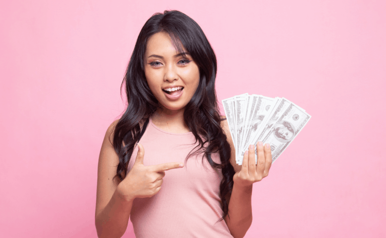 Portrait of young asian woman showing bunch of money banknotes on pink background